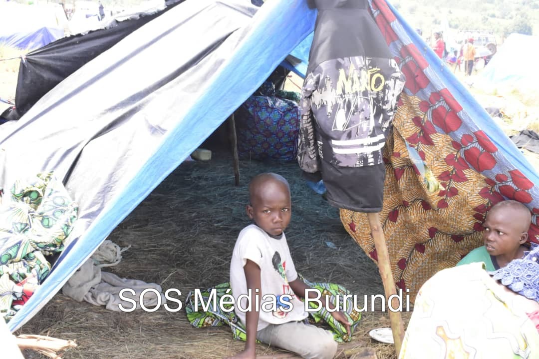 Deux enfants se tiennent devant un abri de fortune, construit avec des pagnes et des bâches en mauvais état, dans le camp de Busuma, à l’est de la petite nation de l’Afrique de l’Est. ©SOS Médias Burundi